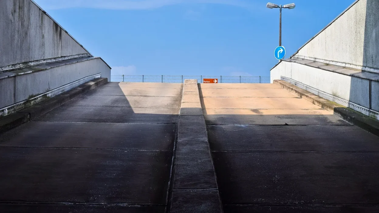 Close-up of dark oil stains on a gray concrete driveway with cleaning supplies nearby.